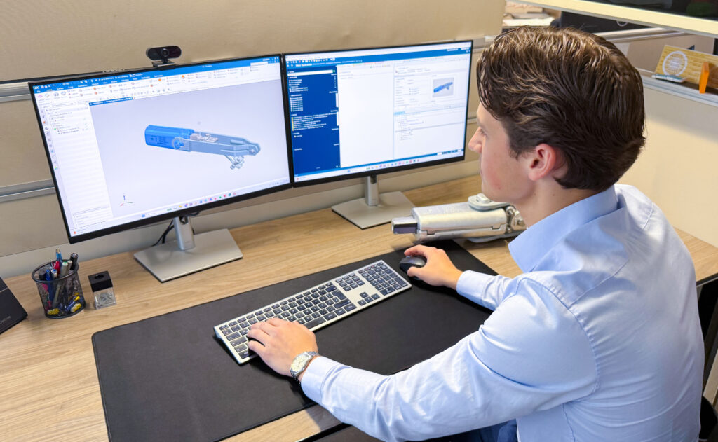 Mitarbeiter sitzt an einem Schreibtisch vor zwei Monitoren und arbeitet mit einer CAD-Software an der 3D-Konstruktion eines technischen Bauteils.